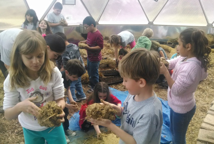 Students handle straw and compost inside the geodesic Growing Dome greenhouse