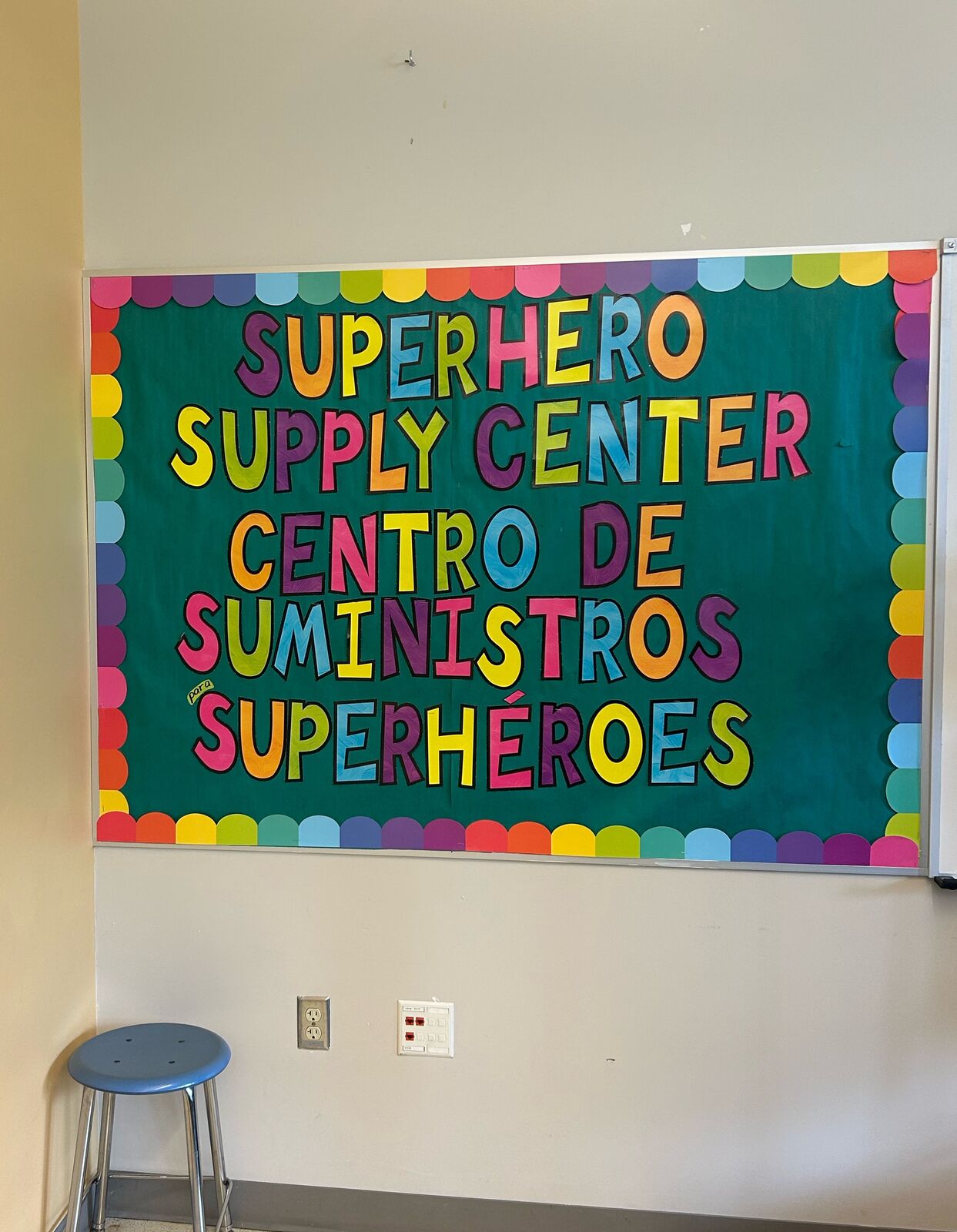 Un tablero de colores que dice Superhero Supply Center y Centro de Suministros Superhéroes